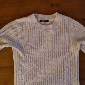 Ljusgrå kabelstickad tröja Gina Tricot - Supersnygg ljusgrå kabelstickad tröja från Gina Tricot. Tröjan har rund halsringning, lång ärm och ett klassiskt kabelmönster som ger en stilren vibe. Perfekt att matcha med jeans eller kjol för en chill look.