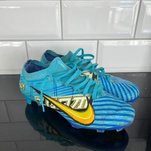 Nike Mercurial Zoom fotbollsskor blå/gul - Säljer ett par Nike Mercurial Zoom fotbollsskor i blått med gula och svarta detaljer. Skorna har snörning, coolt grafiskt mönster och en sula med Zoom-teknologi i blått och gult. Ovandelen är i syntetmaterial och mesh för lätt känsla på planen.