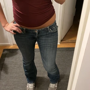 Blå bootcut jeans låg midja - Säljer ett par blå jeans med bootcut och låg midja. Jeansen har klassisk femficksdesign, snygga slitningar och är i ett mjukt denimtyg. Perfekta för dig som gillar en avslappnad men ändå trendig look. Sudda Lågmidjade och har spretats upp, syns inte när de är på. Hålet är förtäckt! Kolla bild.