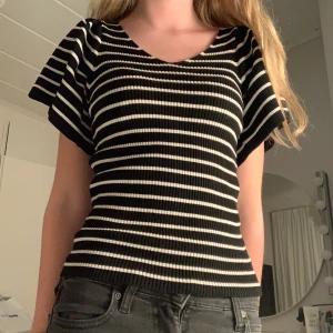 Randig svartvit ribbad topp med knyt - Säljer en svart och vit randig topp med ribbad struktur och korta ärmar. Toppen har en snygg v-ringning framtill och en öppen rygg med knytband. Materialet är stretchigt och sitter snyggt mot kroppen. Säljer pga av att den inte kommer till användning💞 Fint skick, endast använd ett fåtal gånger💓Tveka inte om frågor!