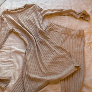 Beige ribbade leggings och långärmad topp-set oanvänd  - Säljer ett set med ribbade leggings och matchande långärmad topp i beige. Byxorna är tighta och stretchiga med hög midja och mjuk känsla, perfekta för en chill och snygg look. Materialet är stickat och ger en mysig vibe.