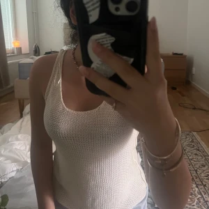 Stickad vit linnetopp - Säljer en stickad vit linnetopp med breda axelband och rundad halsringning. Toppen är ärmlös och har en luftig, mesh-liknande struktur som passar perfekt till varma dagar. Enkel och stilren design som är lätt att matcha med olika outfits.