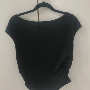 Svart kortärmad topp med twistdetalj - En svart, stilren topp med korta ärmar och en snygg twistdetalj i sidan.  Priset går och diskuteras!  Storlek XL men passar även L och M. (Tröjan är helt ny och aldrig använditis.)