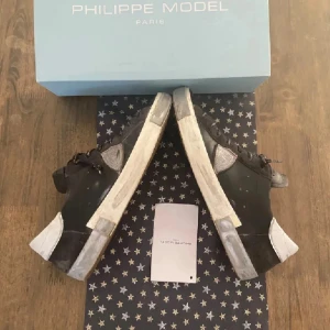 Philippe Model Sneakers - Säljer ett par Philippe Model Prsx Low-Top Sneakers i svart/silver, storlek 44. Stilrena och unika med vita detaljer, silverpatch och text på snörena. Tillverkade av 100 % kalvskinn. Made in Italy. Nypris: 3200 kr.