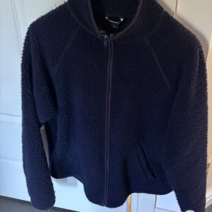Mörkblå teddyjacka Monki  - Bra skick! Lite defekt i krage. Mörkblå teddyjacka från Monki med hel dragkedja framtill och två fickor. Jackan har lång ärm med tumhål och är tillverkad i fluffigt fleece-material. 