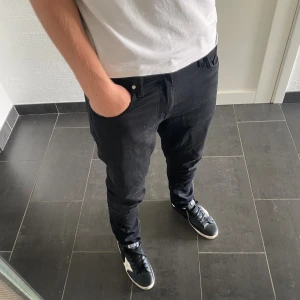 Svarta Tiger of Sweden jeans 31/30 - Säljer ett par svarta jeans från Tiger of Sweden, modell Pistolero. Jag är 185 och väger 77 De har en slim passform med raka ben och klassisk femficksdesign. Jeansen är tillverkade i bomull och har snygga svarta detaljer. Perfekta för dig som gillar stilrena och moderna byxor.