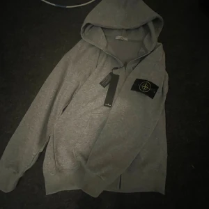 Stone Island kofta - Grå hoodie från Stone Island, köpt från vinted för 1600kr inte helt säker om den är äkta men qr koden säger det direkt storlek s men passar nog m ganska bra också, helt ny med prislapp, pris kan diskuteras, skickar samma dag eller dagen efter 