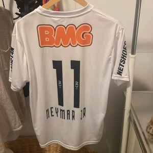 Vit Santos Neymar Jr fotbollströja Nike. - Säljer en vit Santos fotbollströja från Nike med Neymar Jr och nummer 11 på ryggen. Tröjan har tryckta sponsorer, klubbmärke och Dri-FIT-material som andas. Perfekt för dig vill ha en ikonisk tröja på dig!