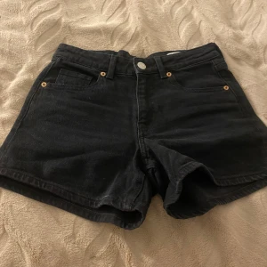 Svarta jeansshorts från Vero Moda XS - Svarta jeansshorts från Vero Moda i klassisk femficksmodell. De är högmidjade med knapp och dragkedja framtill, bälteshällor och raka ben. Perfekta för sommaren och lätta att matcha med allt. Materialet är slitstarkt denim i bomull.