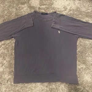 Lila långärmad tröja från Polo Ralph Lauren - Säljer en stilren lila långärmad tröja från Polo Ralph Lauren med klassisk rund halsringning och broderad logga på bröstet. Perfekt för dig som gillar enkel och snygg design. Passar till många olika outfits!