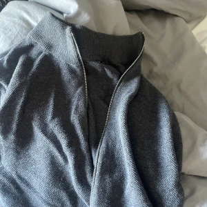 Mörkgrå stickad half zip-tröja - Mörkgrå stickad tröja med half zip och hög krage. Tröjan har en klassisk, enkel design och är perfekt för lager-på-lager. Materialet är mjukt och ribbstickat vid kragen för extra komfort.