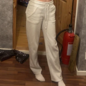 Vita mjukisbyxor med snörning - Säljer ett par vita mjukisbyxor med resår i midjan och snörning. Byxorna har raka ben och stora fickor framtill. Perfekta för en chill och avslappnad stil.