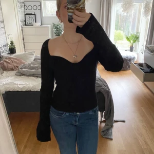 Svart ribbad topp från H&M - Svart långärmad topp från H&M med djup v-ringning och figurnära passform. Toppen är ribbad och har långa, lite utsvängda ärmar. Perfekt att styla med jeans eller kjol för en snygg look.