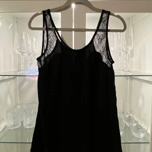 Svart linnetopp med spets från Vila - Snygg svart linnetopp från Vila i storlek XS. Toppen har tunna axelband och detaljer i transparent spets vid axelpartiet som ger en cool och feminin vibe. Materialet är mjukt och lätt, perfekt för att styla med jeans eller kjol. Enkelt att matcha och passar till många looks.