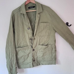 Grön overshirt från J.Lindeberg - Snygg ljusgrön overshirt från J.Lindeberg med klassisk krage och tre stora fickor framtill. Jackan har knäppning med knappar och är långärmad. Perfekt för lager-på-lager och chill stil.