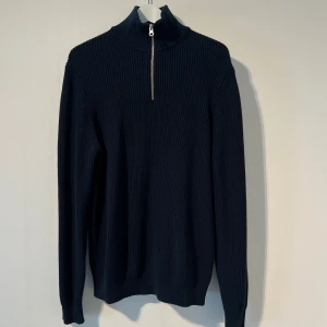 Mörkblå stickad half zip-tröja Zara - Mörkblå stickad tröja från Zara med hög krage och half zip-dragkedja. Tröjan har ribbad struktur och långa ärmar, perfekt för kyligare dagar. Enkel och stilren design som funkar till det mesta. Andvänd 1 gång.
