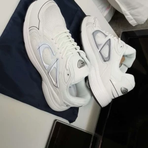 Vita Dior B30  - Säljer ett par vita Dior B30 sneakers med silverdetaljer och reflekterande logga på sidan. Skorna har en chunky sula, snörning och meshpaneler för extra andningsförmåga. Snygg sportig look med exklusiv känsla, perfekt för dig som gillar statement sneakers.