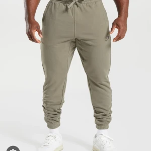 Gymshark Essential Oversized Joggers - Linen Brown - Olivgröna mjukisbyxor från Gymshark med elastisk midja och dragsko. Byxorna har oversized fit. De är bra skick 8/10.