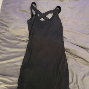 Svart kort klänning Gina Tricot S - Svart kort klänning från Gina Tricot i storlek S. Klänningen har smala axelband som korsas i ryggen och en snygg öppen ryggdetalj. Tillverkad i mjukt bomullsmaterial som sitter skönt och följer kroppen. Perfekt för dig som gillar stilrena och enkla plagg med en twist.