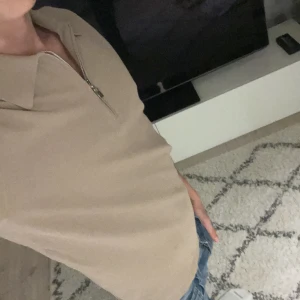 Beige t-shirt med dragkedja Tiger of Sweden - Snygg beige t-shirt från Tiger of Sweden med klassisk krage och halv dragkedja framtill. Passformen är normal och färgen är neutral vilket gör den enkel att matcha. Nypris ca 900 och plagget saknar helt defekter!