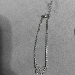 Glittrigt armband med fjäril - Snyggt armband i silverfärg med glittrande stenar och en öppen fjärilsberlock i mitten. Kedjan är täckt av små gnistrande stenar som ger en lyxig känsla. Perfekt accessoar för att lyfta din outfit med lite extra bling.