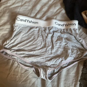 Grå shorts från Candyshion med resår - Mjuka grå shorts från Candyshion med bred vit resår i midjan och svart logga. De är tillverkade i viskos och elastan, vilket gör dem riktigt stretchiga och sköna. Perfekta för att chilla hemma eller till träning.