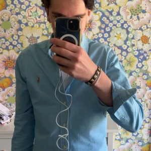 Blå slim fit skjorta från Ralph Lauren - Snygg ljusblå skjorta från Ralph Lauren i slim fit-modell. Klassisk button-down krage, broderad logga på bröstet och vita. Obs notera några väldigt små fläckar (två sista bilderna) Skirv vid funderingar! 