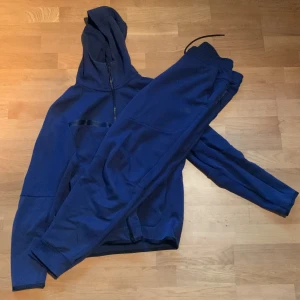 Nike tech fleece navy set - Snygga blå mjukisbyxor med elastisk midja och dragsko. Byxorna har smal passform och muddar vid bensluten. Perfekta för chill eller träning. Byxorna är L och tröjan är M. Lätt slitning på bege plaggen(syns på bild). Skriv vid minsta lilla fundering!