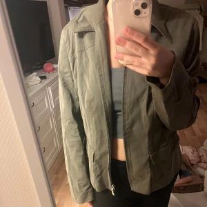 Olivgrön jacka med dragkedja - Säljer en olivgrön jacka med klassisk krage och raka linjer. Jackan har dragkedja framtill, två fickor med lock och är långärmad. Materialet känns som bomull eller polyester och passformen är normal. Perfekt för dig som gillar stilren och enkel look.