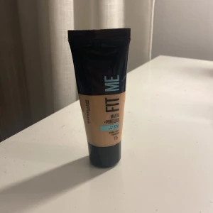 Maybelline Fit Me Matte Foundation 115 - Maybelline Fit Me Matte + Poreless Foundation i nyansen 115. Kommer i en smidig tub med svart och beige design och blå text. Ger en matt finish och jämnar ut huden. Passar normal till oljig hud och håller upp till 12 timmar.
