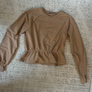 Beige långärmad tröja från NA-KD - Aldrig använd, super fin på verkligen men kommer ej till användning. Säljer en beige långärmad tröja från NA-KD i storlek M. Tröjan har rund hals, smock vid midjan som ger en snygg volangkant och elastiska muddar vid ärmslut. Perfekt för dig som gillar enkel och stilren design.🥰🥰