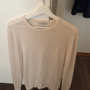 Beige stickad tröja Tiger of Sweden - Snygg beige stickad tröja från Tiger of Sweden med rund hals och långa ärmar. Tröjan har en clean look och är tillverkad i mjukt material som känns skönt mot huden. Perfekt för dig som gillar stilrena och enkla plagg.