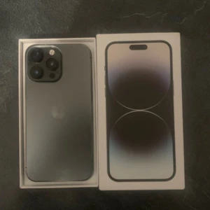 iPhone 14 Pro - Snygg iPhone 14 Pro i svart, säljs med originalkartong. Telefonen har trippelkamera och ser ut att vara i mycket gott skick utan synliga repor eller skador. Perfekt för dig som vill ha en kraftfull och stilren smartphone med avancerad kamera och hög prestanda.