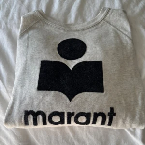 Grå sweatshirt från Isabel Marant - Grå sweatshirt från Isabel Marant med stort svart logotryck framtill. Tröjan är i helt okej skick, den har en liten liten fläck som man ser i andra bilden. Säljer då den inte kommer till andvändning längre. (Pris kan diskuteras)