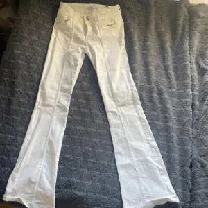 Vita bootcut jeans med låg midja - Snygga vita bootcut jeans med bootcut och låg midja. Byxorna har dubbla knappar och markerad söm längs benen. 