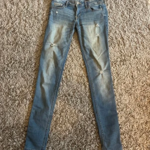 Ljusblåa  jeans från Hollister - Snygga ljusblå jeans från Hollister med slitningar på benen och coola broderade bakfickor. Klassisk femficksmodell med låg midja och dragkedja. Perfekta för dig som gillar en detaljerad look.