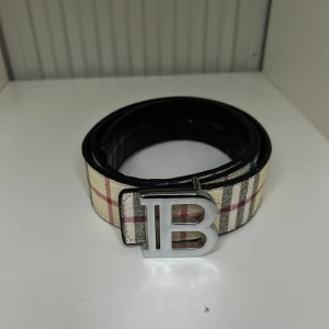 Burberry bälte - Snyggt bälte från Burberry med klassiskt rutmönster i beige, svart mönster som går och ändra vilken färg man vill ha som ger en lyxig touch på din outfit med en längd på 105cm