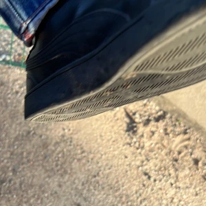 Svarta Puma sneakers i skinn - Säljer ett par svarta Puma sneakers i skinn med klassisk design och svarta snören. Skorna har rund tå och platt sula, perfekt för dig som gillar en clean och stilren look. Puma-loggan syns tydligt på sidan. Passar till jeans och streetwear.