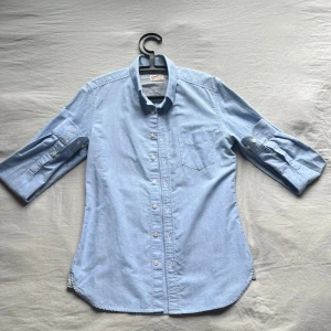 Ljusblå skjorta från Cropp - Ljusblå skjorta från Cropp i bomull med klassisk krage, bröstficka och knappar framtill. Perfekt för en chill och stilren look.