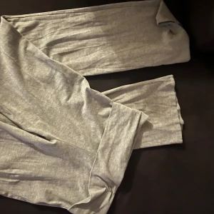 Gråa mjukisbyxor med bred mudd - Säljer ett par ljusgrå mjukisbyxor med bred mudd i midjan. Byxorna är i mjukt bomullsmaterial och har en tight passform som sitter skönt mot kroppen. Perfekta för chill dagar hemma eller när du vill ha det extra bekvämt.