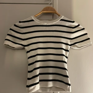 Randig topp från Gina Tricot XS - Säljer en vit och svart randig topp från Gina Tricot i storlek XS. Toppen har korta ärmar, rund halsringning och är tillverkad i ett mjukt, ribbat material. Perfekt för en stilren och klassisk look.