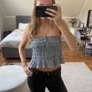 Rutig blåvit croppad linnetopp från Ginatricot - Supersöt croppad linnetopp med blåvitt rutigt mönster och smala axelband från Ginatricot. Toppen har volangkant nertill och en liten knytning framtill. Perfekt för varma dagar och ger en fräsch sommarkänsla.