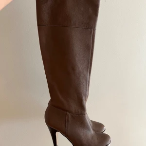 Bruna höga stövlar från Topshop strl 39 - Snygga bruna stövlar i äkta skinn med 9cm hög klack och rund tå. Stövlarna har dragkedja på insidan för enkel påtagning och en stilren, klassisk design. Perfekta för att lyfta din höst- eller vinterlook.