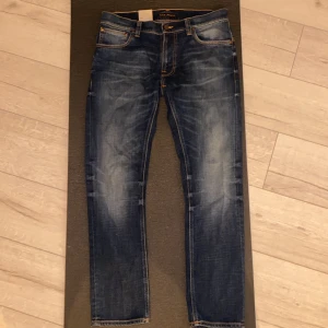 Nudie Jeans Thin Finn Indigo Dreams W32 - Snygga blå jeans från Nudie Jeans, modell Thin Finn Indigo Dreams. Jeansen har en smal passform, klassisk femficksdesign och är tillverkade av 100% ekologisk bomull. Färgen är mörkblå med slitningar och kontrastsömmar. Perfekta för en avslappnad och trendig look. Näst intill sprillans nya, delar av tags kvar. 