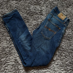Nudie Jeans - Nudie Jeans med lite slitningar i storlek 29/32! Använda och vissa slitage (baksida) som syns på bild 2. Skriv till mig vid frågor eller funderingar!