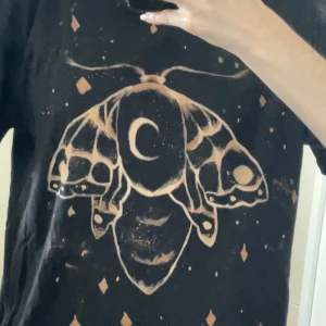  t-shirt med mal/moth -  svart t-shirt med handblekt motiv av en mal. Baggy t-shirt, passar S-M