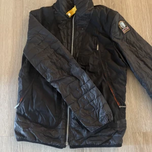 Svart lättviktsjacka från Parajumpers - Svart lättviktsjacka från Parajumpers med klassisk patch på ärmen och cool gul detalj vid kragen. Jackan har dragkedjor på fickorna och framtill, samt quiltad look. Perfekt för dig som vill ha en snygg och smidig jacka med streetkänsla. Kan gå ner i pris vid behov 