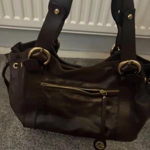 Mörkbrun axelväska  - Snygg mörkbrun axelväska. Perfekt storlek för att få plats med allt du behöver och ger en cool vibe till din outfit. Ordinarie pris:550