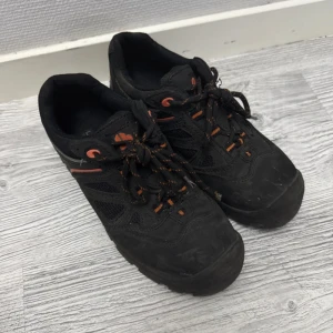 Svarta arbetsskor från L.Brador strl 40 - Svarta arbetsskor från L.Brador med orange detaljer och snörning. Skorna har stålsätta,robust platt sula och är tillverkade i slitstarkt syntetmaterial med meshpaneler för extra ventilation. ISO 20345:2011 S1P