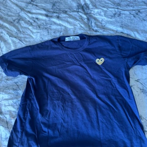 CDG Tshirt - En blå CDG tshirt med ett guldigt hjärta